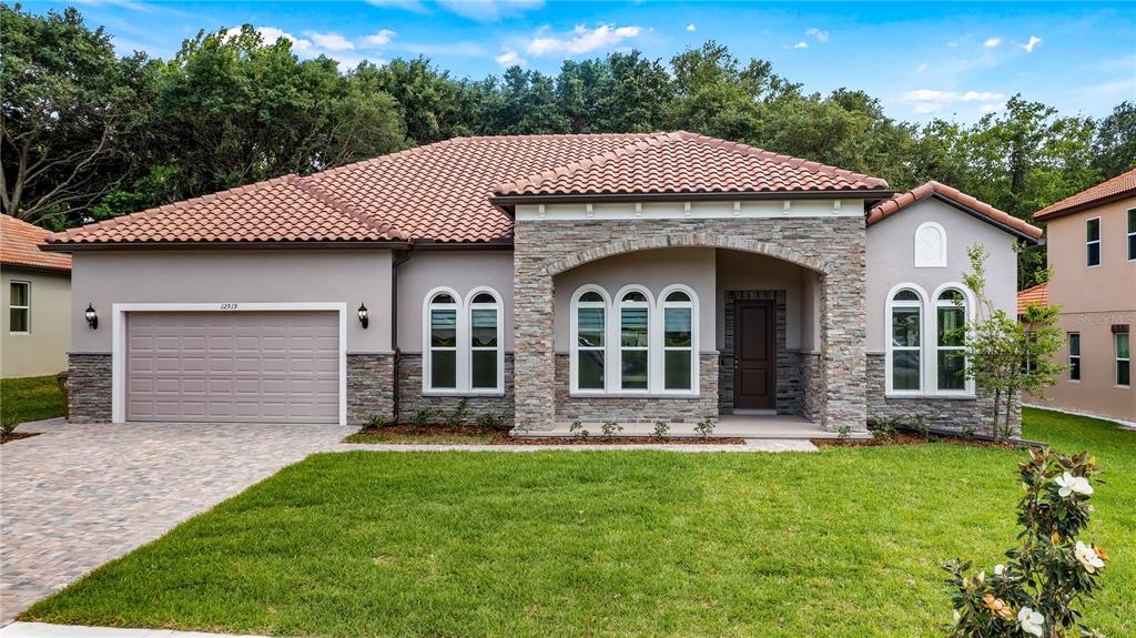 A single-story house with a stone facade, tiled roof, and a paved driveway — 12919 BRUNELLO CIRCLE, CLERMONT, FL
