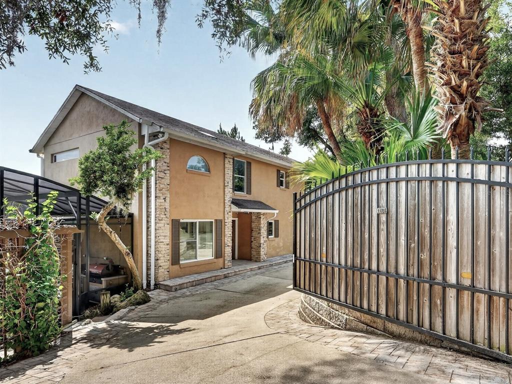 A two-story stucco house with stone accents sits behind a tall wooden gate and fence — 1625 ABRAMS ROAD, EUSTIS, FL