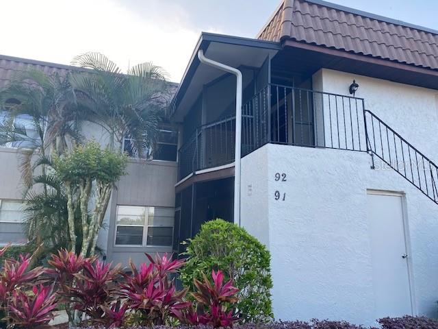 A two-story residential building exterior features white stucco walls, black metal railings, and tropical landscaping — 92 WINDTREE LANE UNIT L, WINTER GARDEN, FL
