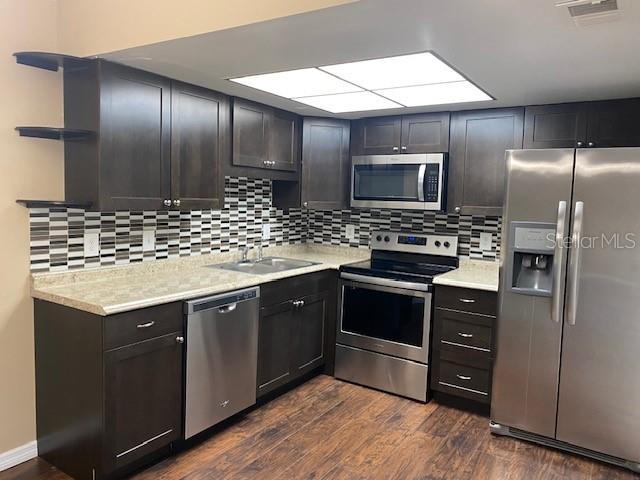A kitchen features dark wood cabinets, stainless steel appliances, and a patterned tile backsplash — 92 WINDTREE LANE UNIT L, WINTER GARDEN, FL