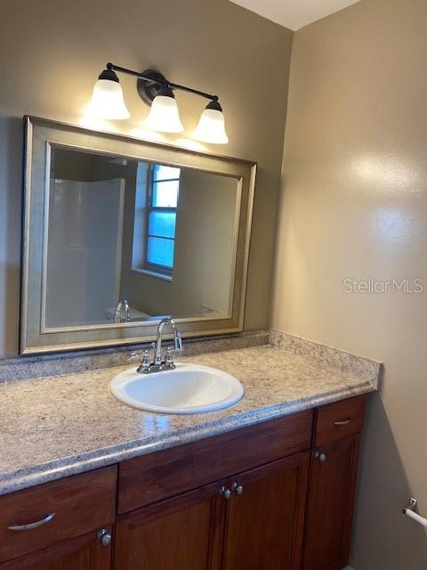 A bathroom features a wood vanity with a granite countertop, a sink, and a framed mirror — 92 WINDTREE LANE UNIT L, WINTER GARDEN, FL