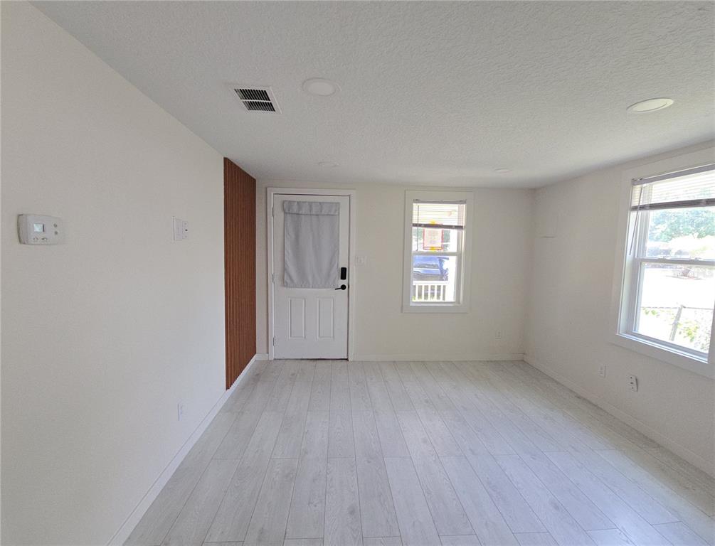 An empty room features light wood-look flooring, white walls, a white door, and two windows — 1626 GAR STREET, ST CLOUD, FL