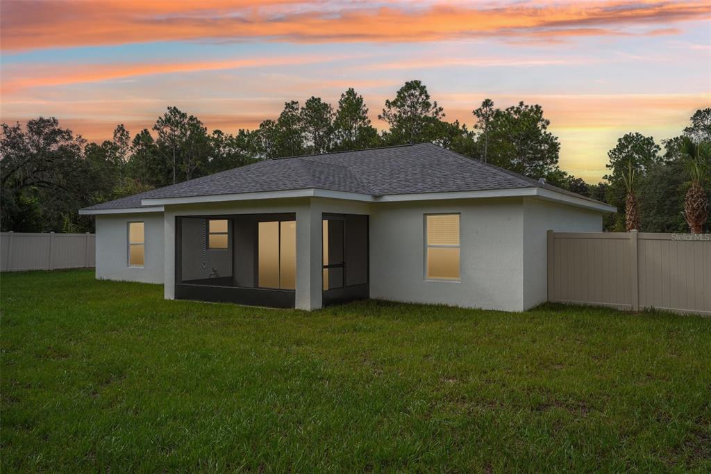 The exterior rear view of a single-story house featuring a screened-in porch and vinyl fencing — 509 W WASON STREET, CITRUS SPRINGS, FL