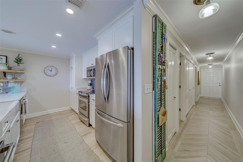 A kitchen with stainless steel appliances and white cabinetry leads into a long hallway — 2250 GULF BOULEVARD UNIT B2, BELLEAIR BEACH, FL