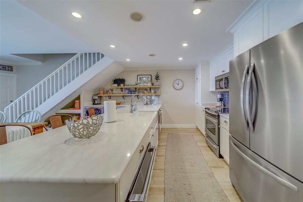 A kitchen features a long white marble island, stainless steel appliances, and an adjacent staircase — 2250 GULF BOULEVARD UNIT B2, BELLEAIR BEACH, FL