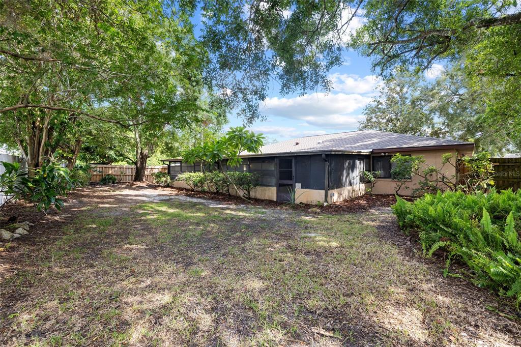 The backyard of a house features a screened-in porch, mature trees, and a wooden fence — 3307 DEL PRADO COURT, TAMPA, FL