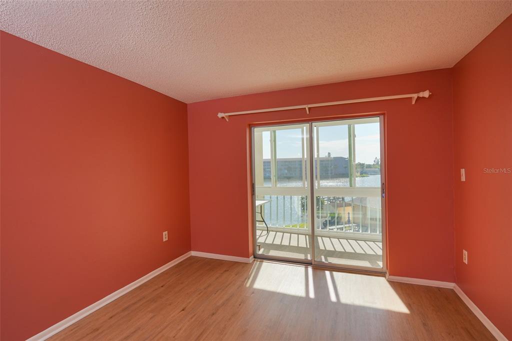 An empty bedroom with coral-colored walls, light wood-look flooring, and a sliding glass door — 3607 LAKE BAYSHORE DRIVE UNIT J-312, BRADENTON, FL
