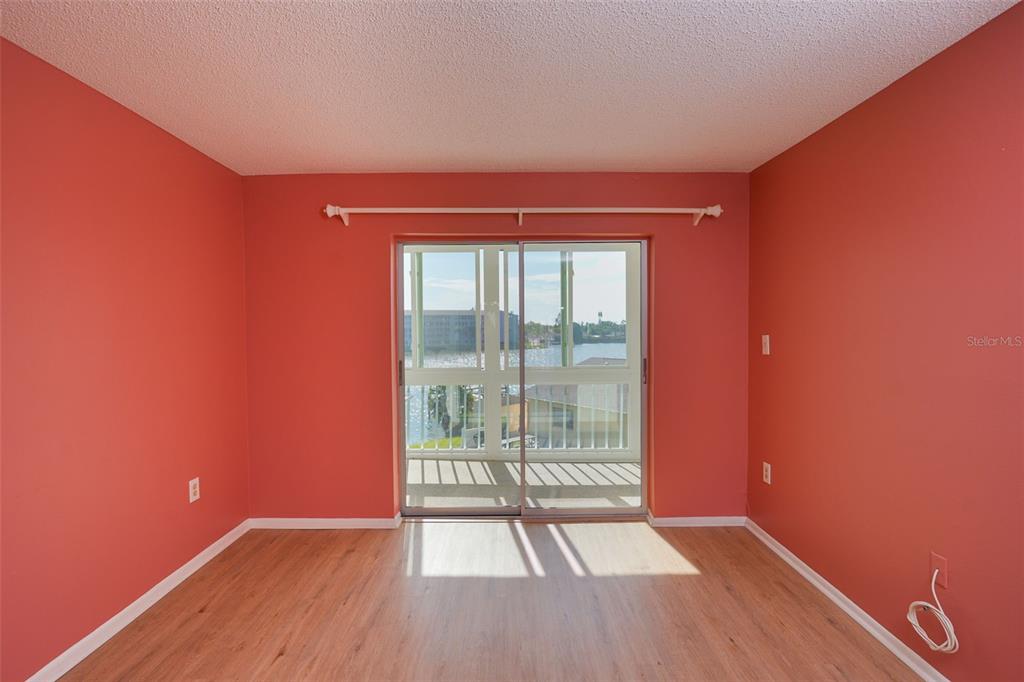 An empty room with coral-colored walls, light wood flooring, and a sliding glass balcony door — 3607 LAKE BAYSHORE DRIVE UNIT J-312, BRADENTON, FL