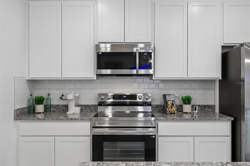 A kitchen features white cabinets, stainless steel appliances, a subway tile backsplash, and granite countertops — 1407 NEEDLE PALM DRIVE, EDGEWATER, FL