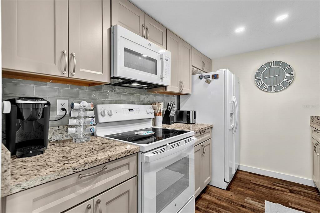 A kitchen features light-colored cabinets, granite countertops, white appliances, and a wall-mounted analog clock — 3600 S OCEANSHORE BOULEVARD, FLAGLER BEACH, FL