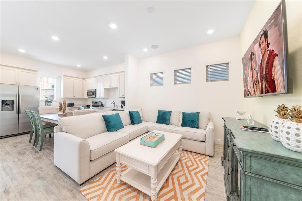 A living room with a sectional sofa, coffee table, and television opens to a kitchen — 8041 LOST SHAKER LANE, KISSIMMEE, FL