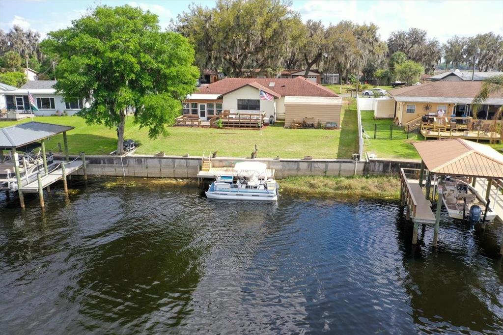 An aerial view shows a waterfront house with a deck, a boat, and boat docks — 9103 E AQUA VISTA DRIVE, INVERNESS, FL