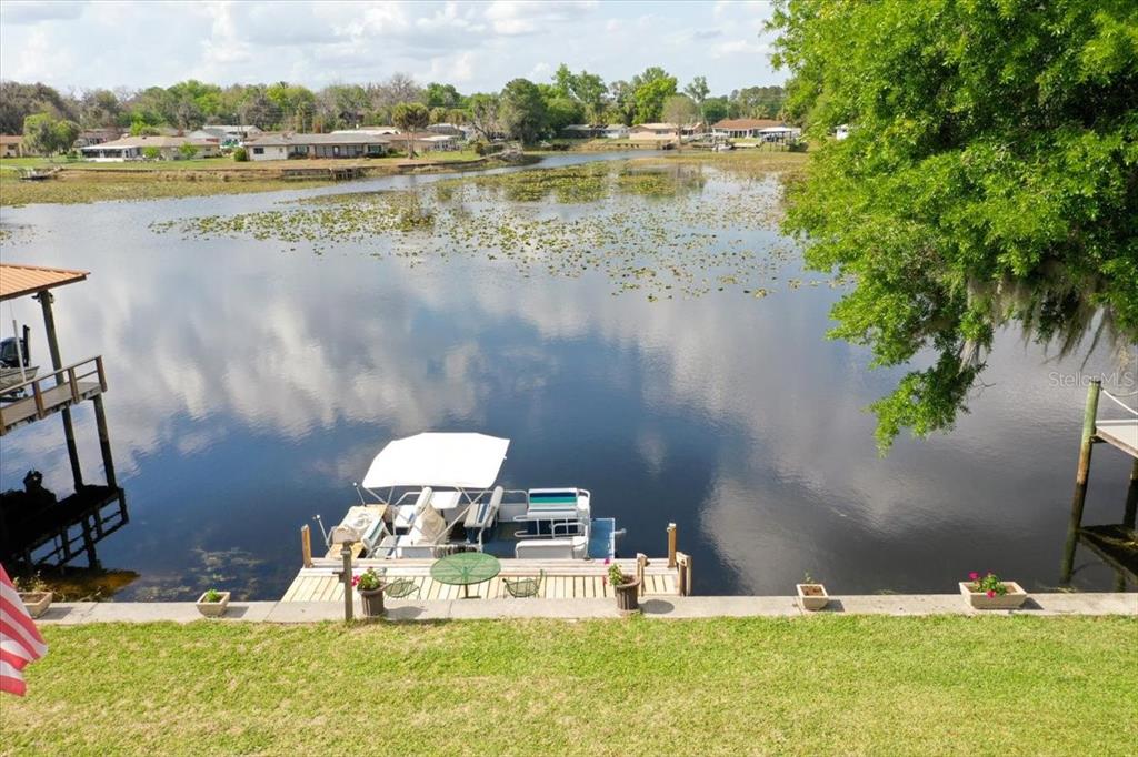 A pontoon boat is docked at a wooden pier on a lake with lily pads — 9103 E AQUA VISTA DRIVE, INVERNESS, FL