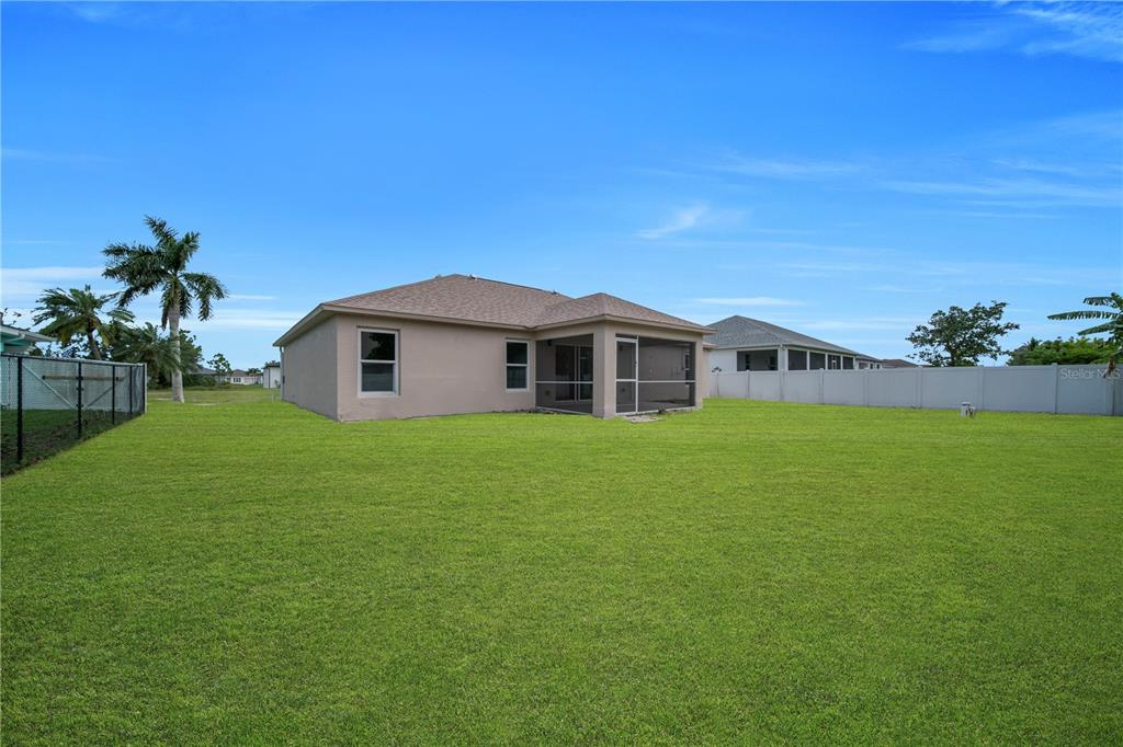 The exterior of a tan house with a screened-in porch sits on a large grassy lawn — 2007 NW 21ST ST, CAPE CORAL, FL
