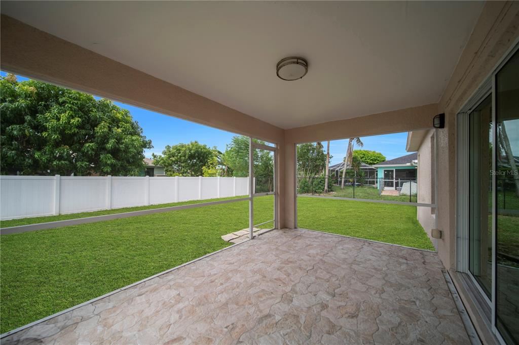 A covered patio with stone-patterned flooring overlooks a fenced backyard through a screened enclosure — 2007 NW 21ST ST, CAPE CORAL, FL