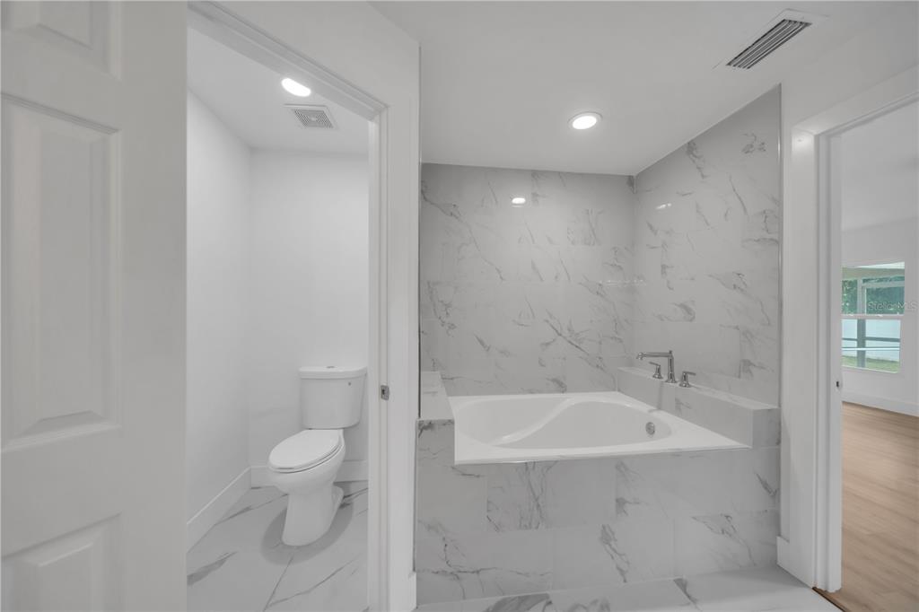A bathroom features a soaking tub with marble-look tile surround and a separate toilet area — 2007 NW 21ST ST, CAPE CORAL, FL