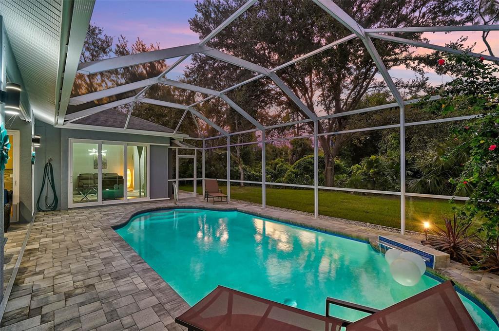 A screened-in swimming pool with a paver patio sits outside a house at sunset — 599 PINE RANCH EAST ROAD, OSPREY, FL