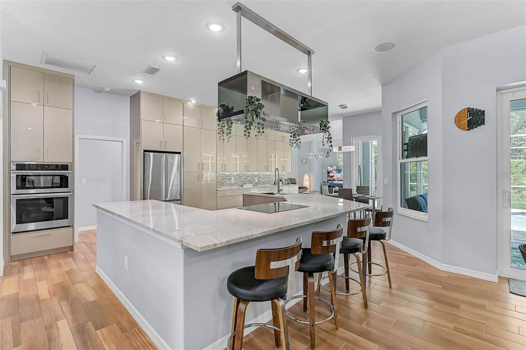 A modern kitchen features light-colored cabinetry, a large marble-topped island with bar stools, and wood flooring — 599 PINE RANCH EAST ROAD, OSPREY, FL