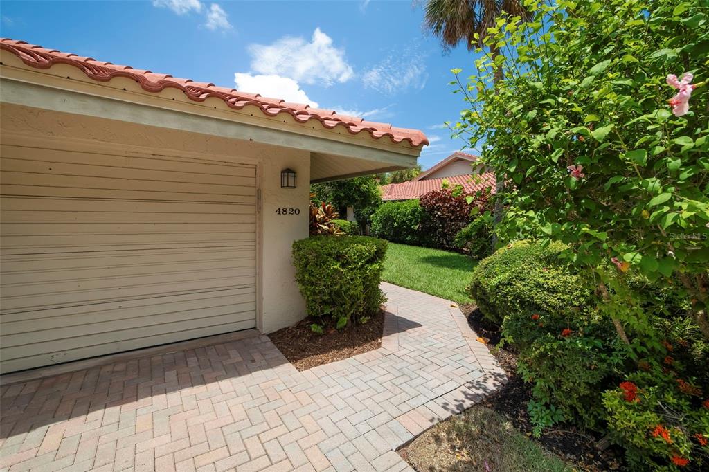 A single-story duplex with a red tile roof and two garage doors faces a driveway — 4820 KESTRAL PARK CIRCLE UNIT 18, SARASOTA, FL