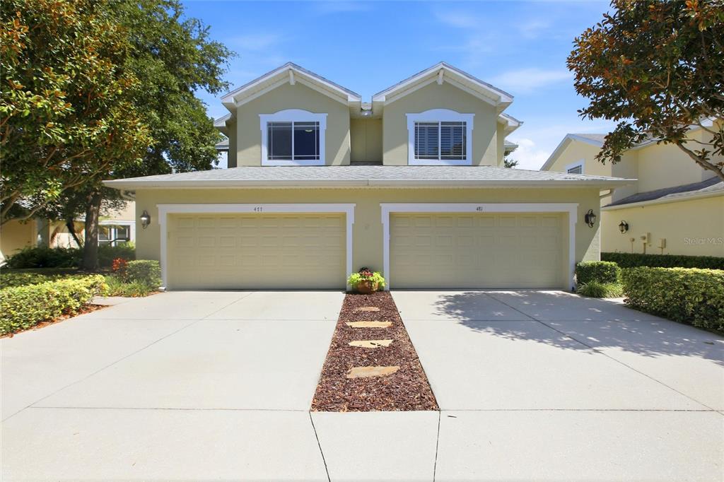 A two-story townhouse exterior features a beige stucco facade, a two-car garage, and a driveway — 477 HARBOR RIDGE DRIVE, PALM HARBOR, FL