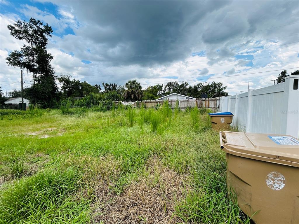 An overgrown grassy lot features two brown trash bins near a white vinyl fence — 1493 TALLAHASSEE BOULEVARD, INTERCESSION CITY, FL