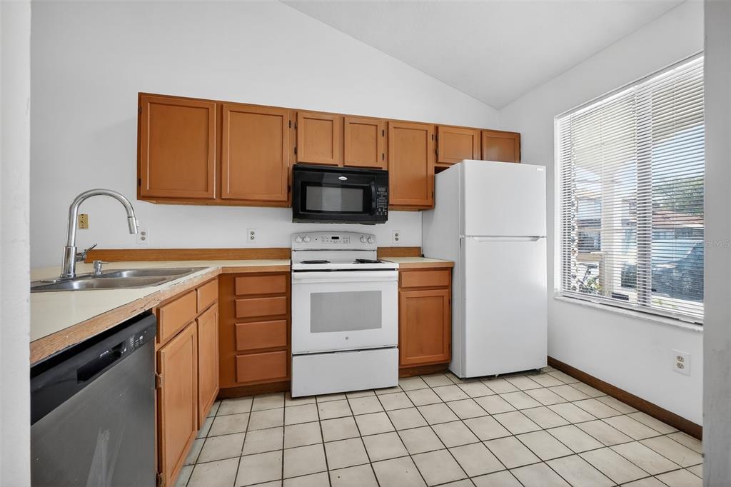 A kitchen with wood cabinets, white appliances, a double sink, and tiled flooring — 3559 FOREST BRANCH DRIVE Apt E, PORT ORANGE, FL