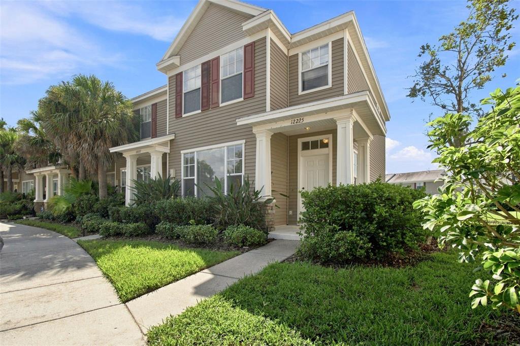 A two-story townhouse with beige siding, a covered front porch, and a landscaped front yard — 12225 COUNTRY WHITE CIRCLE, TAMPA, FL