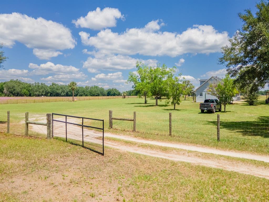 A dirt driveway leads through a metal gate toward a house on a grassy lot — 4381 NE 105TH PLACE, ANTHONY, FL