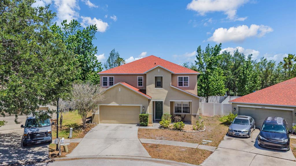 A two-story suburban house with a tan exterior, red roof, and a concrete driveway — 10945 SUBTLE TRAIL DRIVE, RIVERVIEW, FL