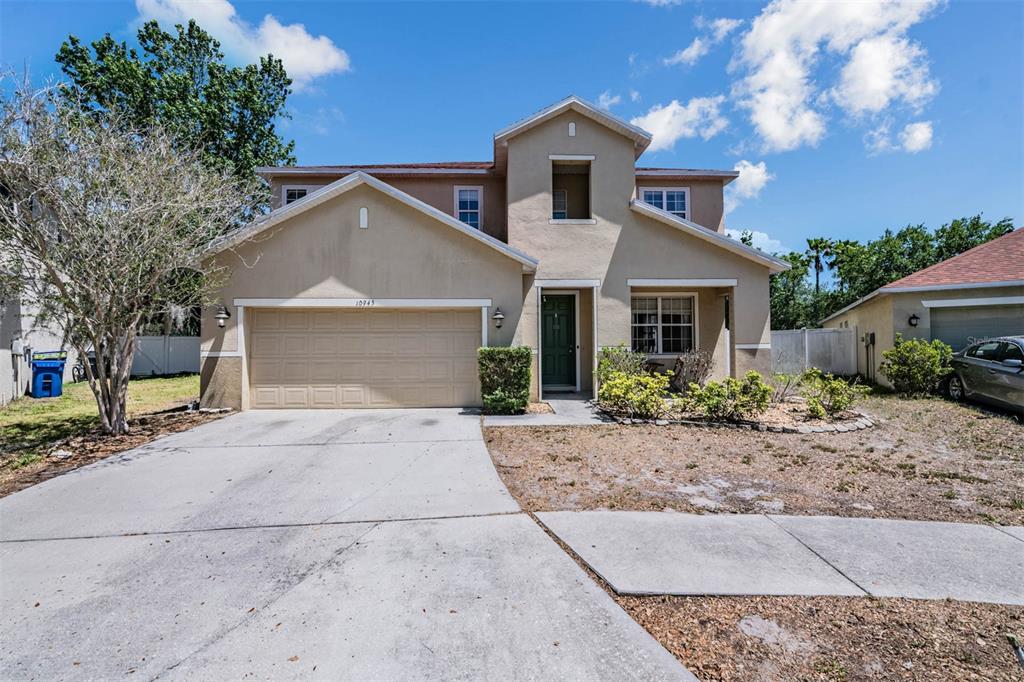 A two-story suburban house with a tan stucco exterior, a two-car garage, and a driveway — 10945 SUBTLE TRAIL DRIVE, RIVERVIEW, FL