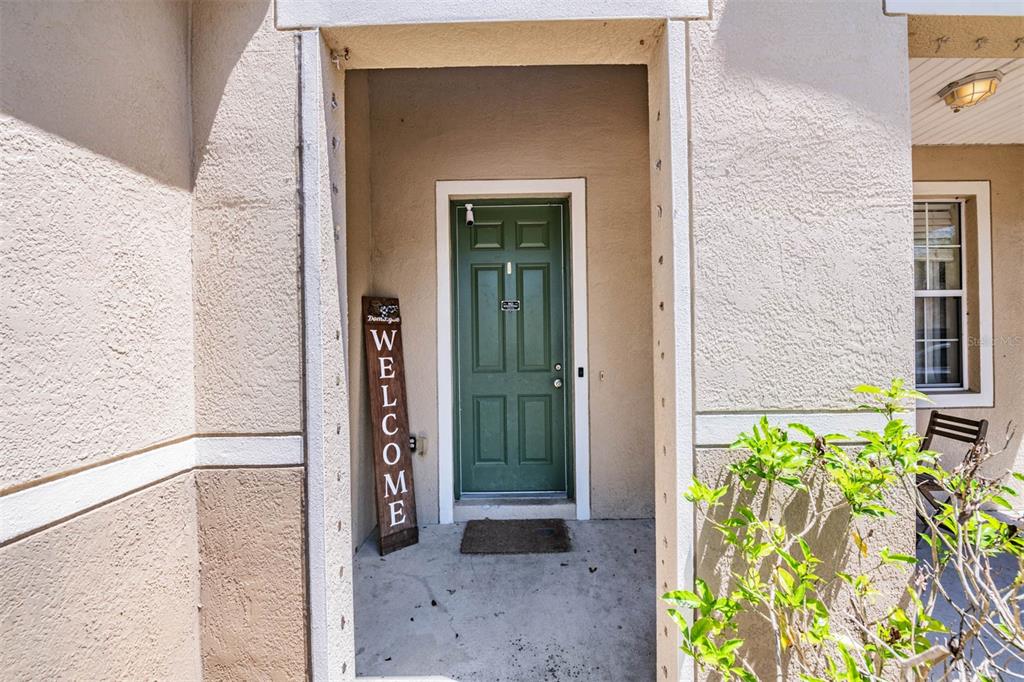 A green front door with a welcome sign sits under a covered entryway — 10945 SUBTLE TRAIL DRIVE, RIVERVIEW, FL