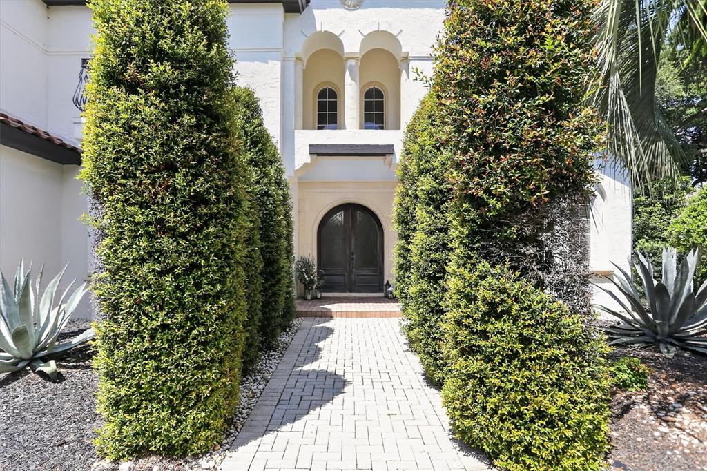 A paved walkway leads to a dark arched front door flanked by tall manicured hedges — 8826 SOUTHERN BREEZE DRIVE, ORLANDO, FL