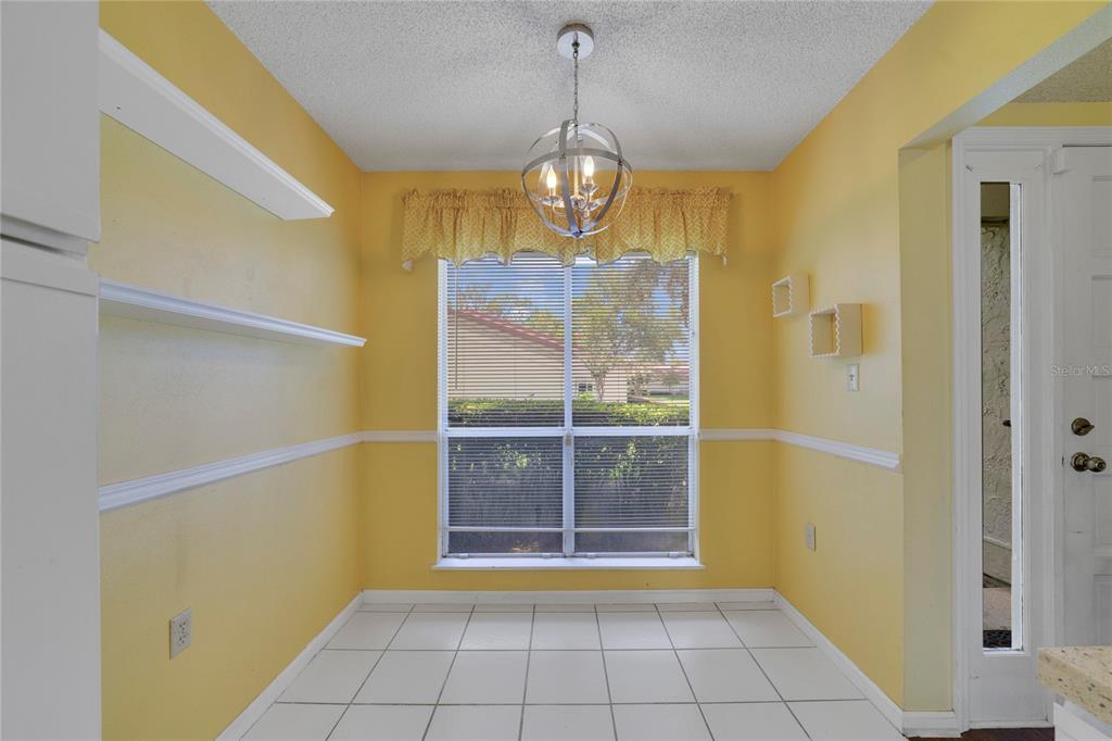 A bright yellow dining nook features white tile flooring, floating shelves, and a globe chandelier — 260 W SABAL PALM PLACE, LONGWOOD, FL
