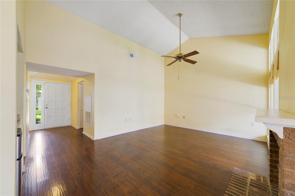 A living room with vaulted ceilings, dark wood flooring, a ceiling fan, and a brick fireplace — 260 W SABAL PALM PLACE, LONGWOOD, FL