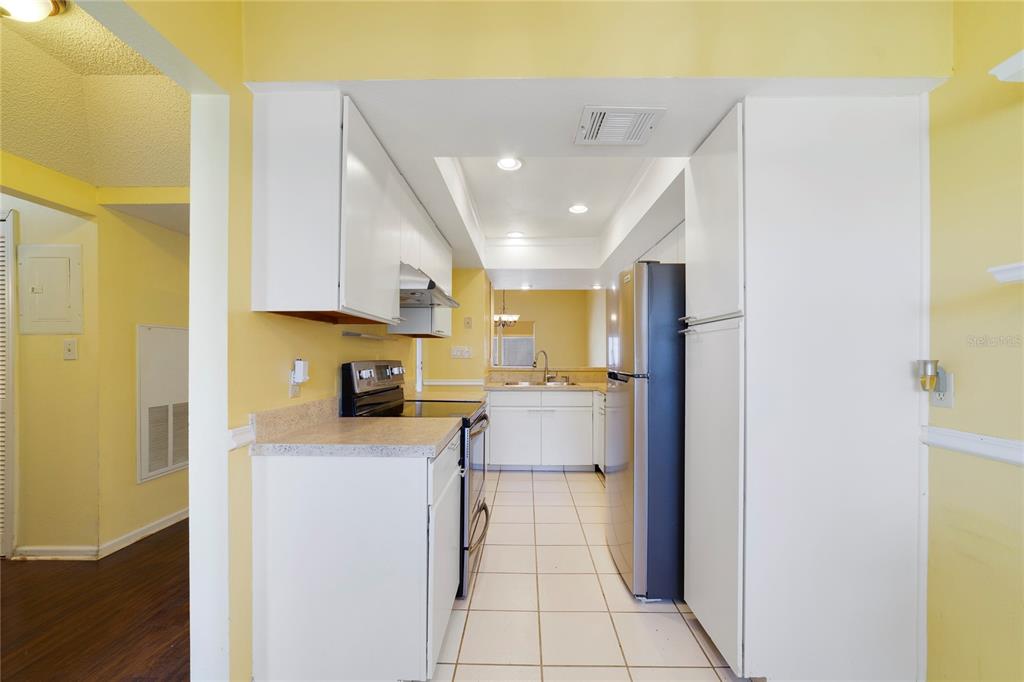 A galley-style kitchen features white cabinets, stainless steel appliances, and light-colored tile flooring — 260 W SABAL PALM PLACE, LONGWOOD, FL
