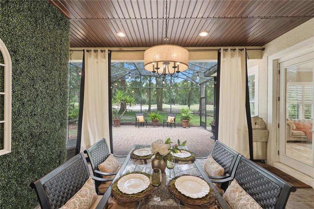 A covered outdoor dining area features a glass table, chandelier, and a view of a patio — 125 ASTERBROOKE DRIVE, DELAND, FL