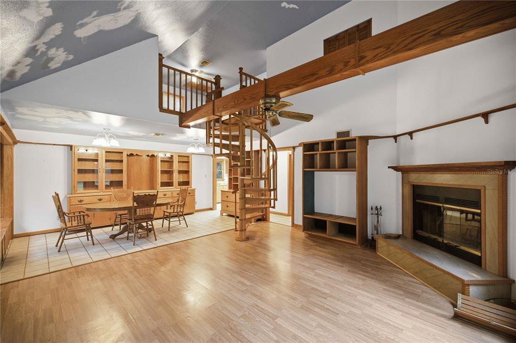 A living room with a spiral staircase, wood flooring, a fireplace, and a dining area — 3580 NE 160TH LANE, CITRA, FL