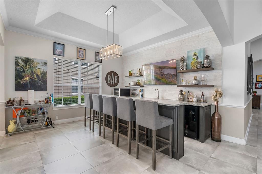 A home bar area features gray cabinetry, a stone accent wall, and four bar stools — 11524 CLAYMONT CIRCLE, WINDERMERE, FL