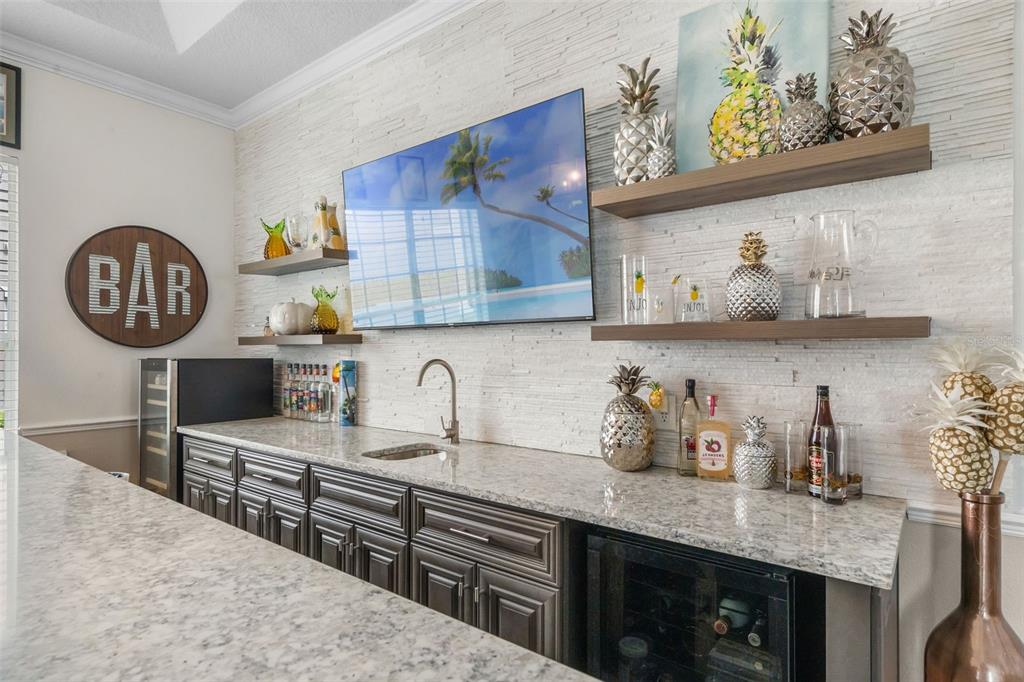 A home bar features dark cabinetry, granite countertops, a sink, and pineapple-themed decor — 11524 CLAYMONT CIRCLE, WINDERMERE, FL