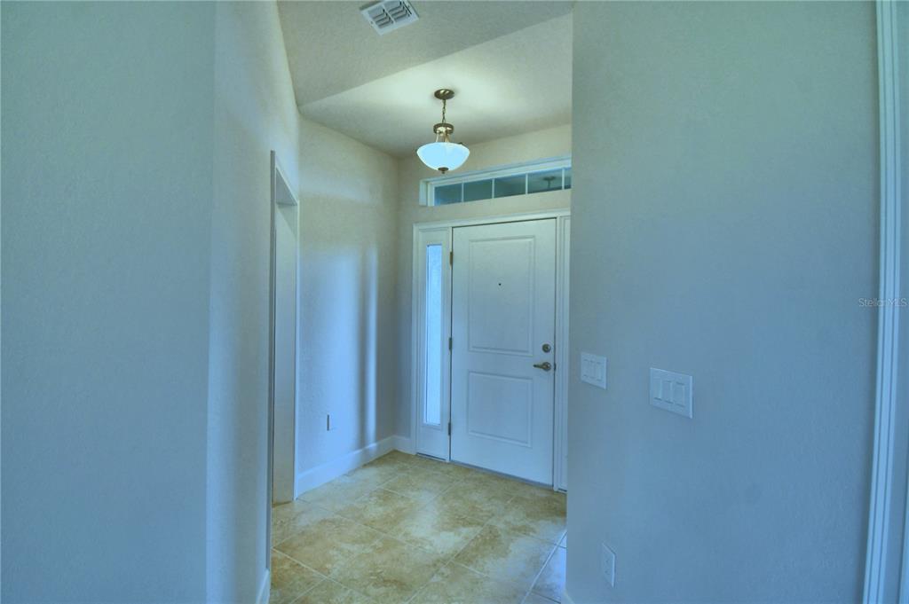 An entryway features light-colored tile flooring, a white front door, and a hanging light fixture — 4628 CALAMINT LANE, AUBURNDALE, FL