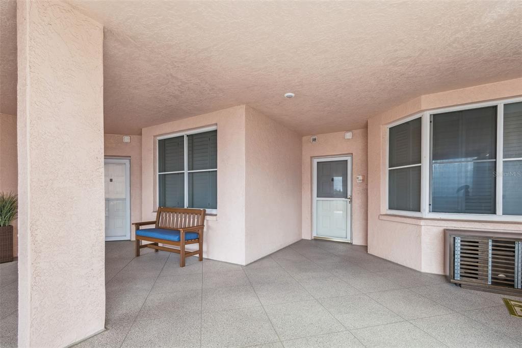 A covered patio features pink stucco walls, a tiled floor, and a wooden bench — 4991 BACOPA LANE S UNIT 502, ST PETERSBURG, FL