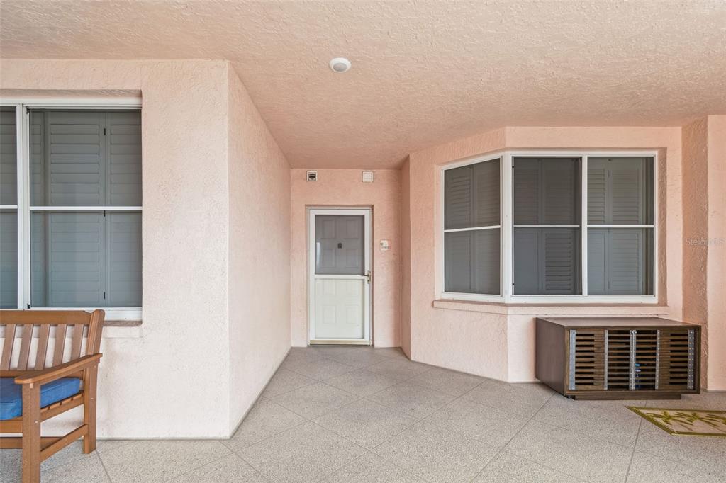 A covered outdoor patio features light pink stucco walls, tile flooring, and a wooden bench — 4991 BACOPA LANE S UNIT 502, ST PETERSBURG, FL