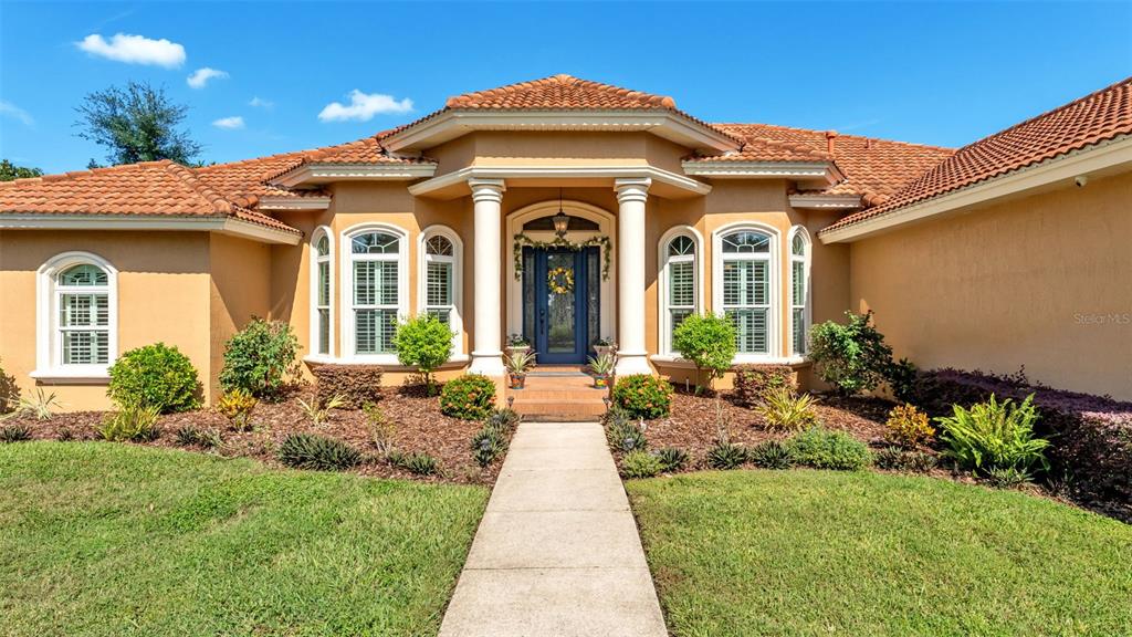 A tan stucco house features a tiled roof, white columns, and a central front entrance — 237 MCLEAN POINT, WINTER HAVEN, FL