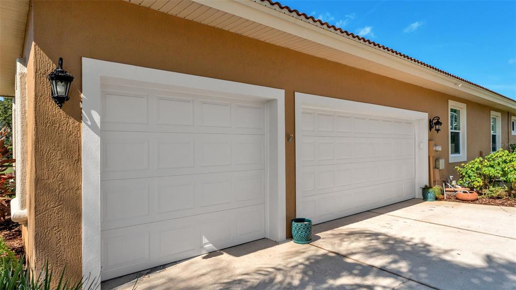 A tan stucco house exterior features two white garage doors and two wall-mounted lanterns — 237 MCLEAN POINT, WINTER HAVEN, FL