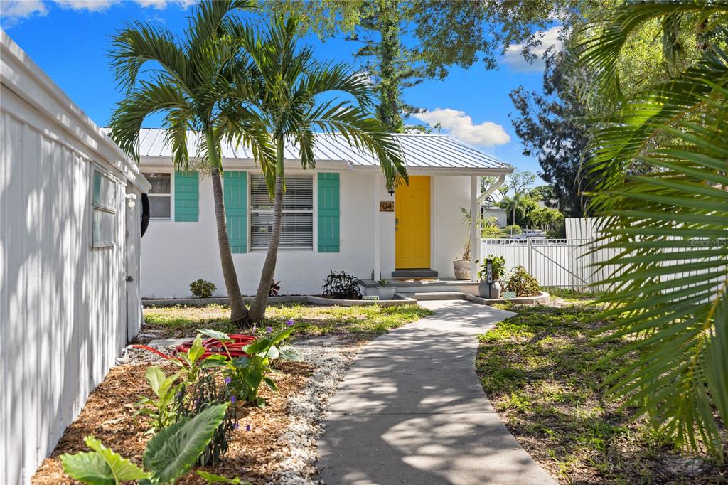 A white house with a yellow front door and turquoise shutters sits behind a walkway — 704 69TH AVENUE W, BRADENTON, FL