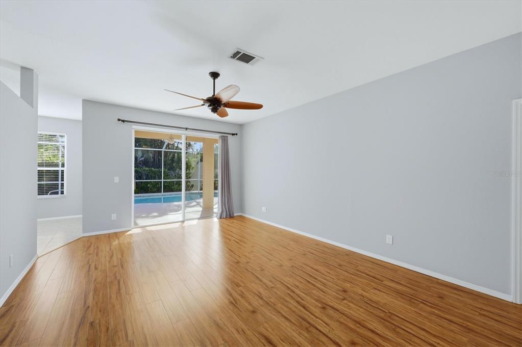 An empty room with wood-look flooring, a ceiling fan, and sliding doors opening to a pool — 5009 46TH STREET W, BRADENTON, FL