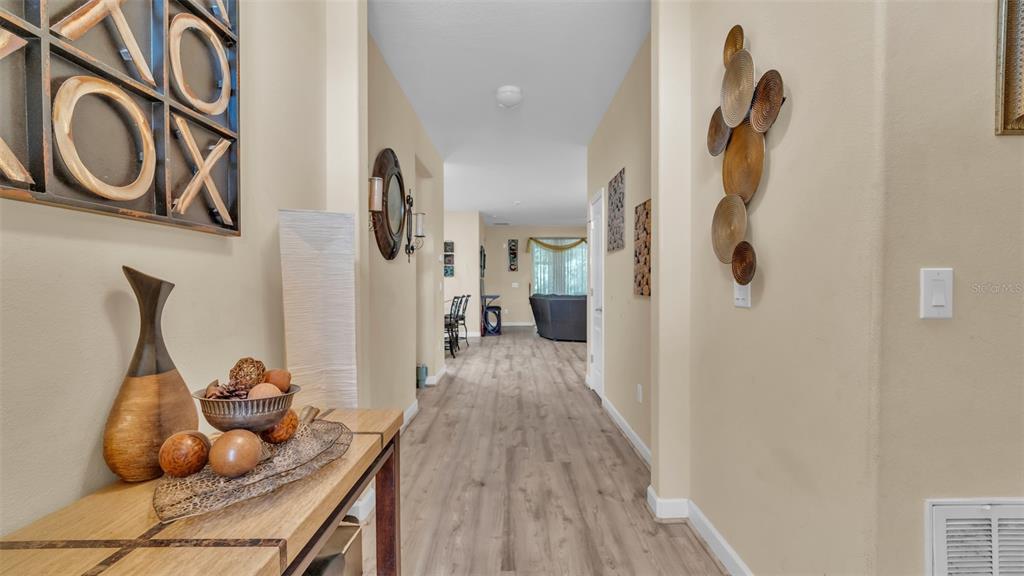A hallway with light wood flooring leads from a foyer into a living area — 12848 WHITE BLUFF ROAD, HUDSON, FL