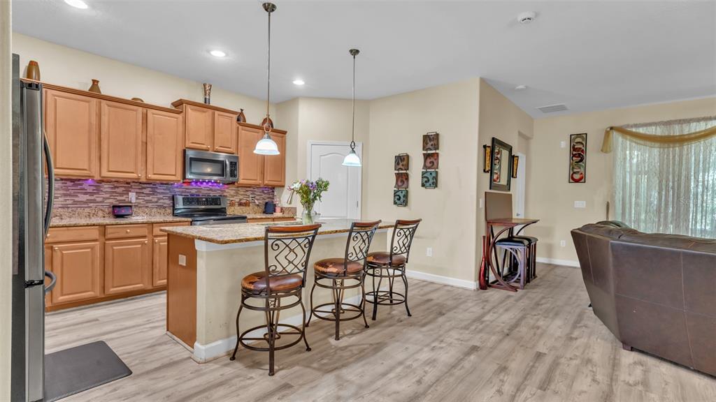 A kitchen with light wood cabinets, granite countertops, and a breakfast bar with three stools — 12848 WHITE BLUFF ROAD, HUDSON, FL