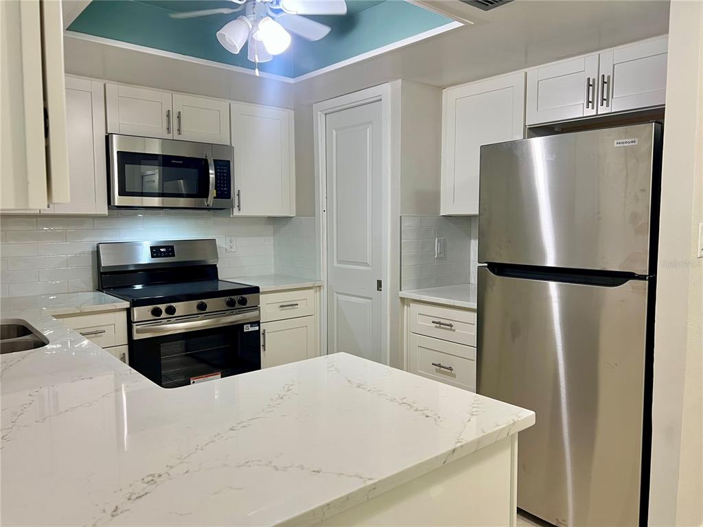A kitchen features white cabinets, stainless steel appliances, and a white marble-patterned countertop — 632 EDGEWATER DRIVE UNIT 139, DUNEDIN, FL