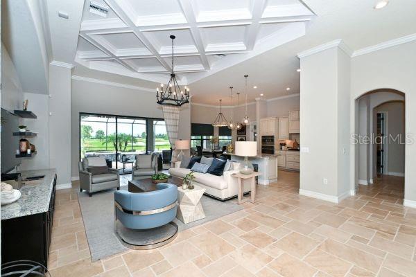 A bright, open-concept living room features a coffered ceiling, tile flooring, and a large chandelier — 5507 ARNIE LOOP, LAKEWOOD RANCH, FL